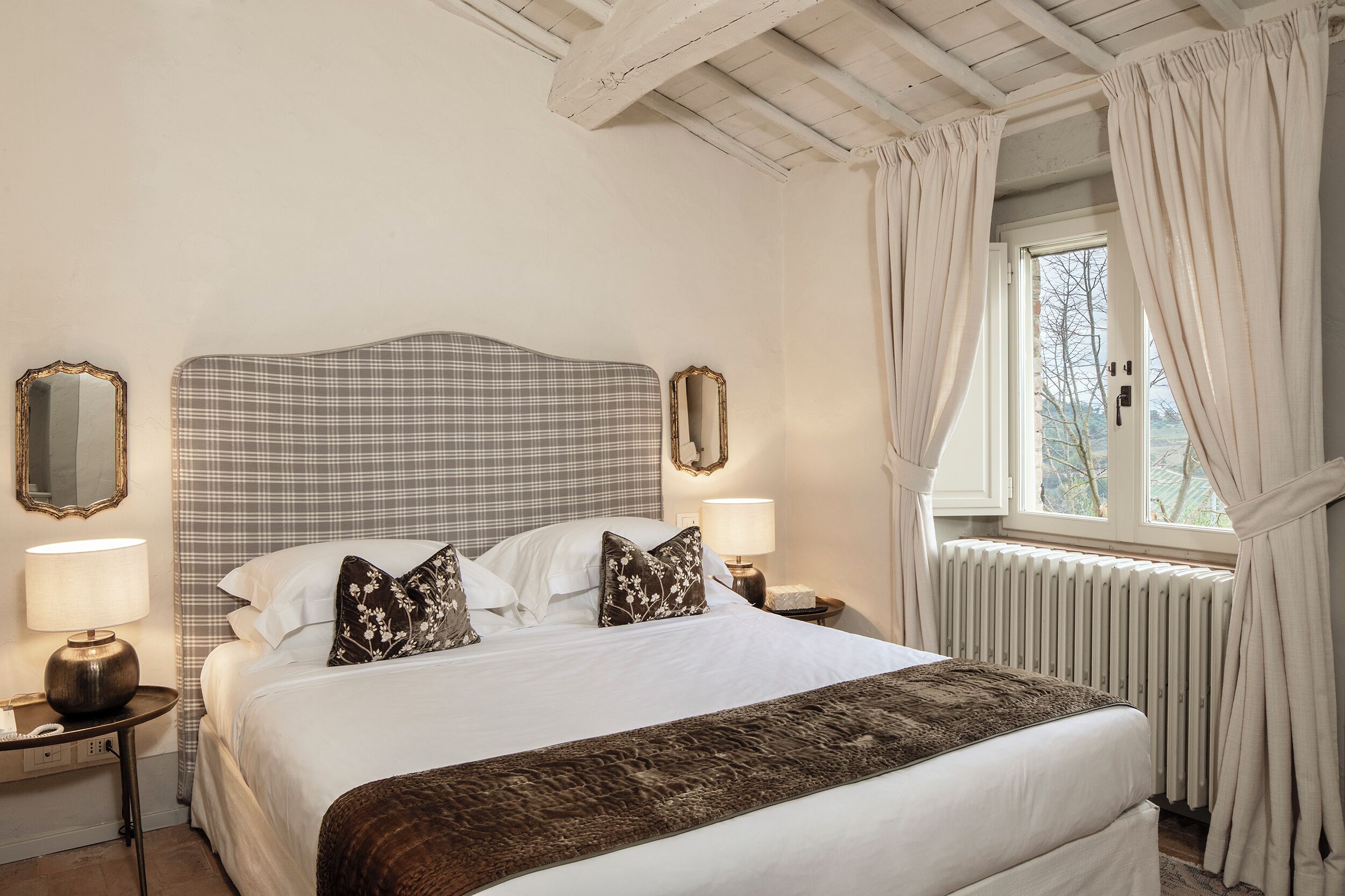 A hotel room with a large bed, two bedside tables with lamps, a mirror, and a window with curtains.