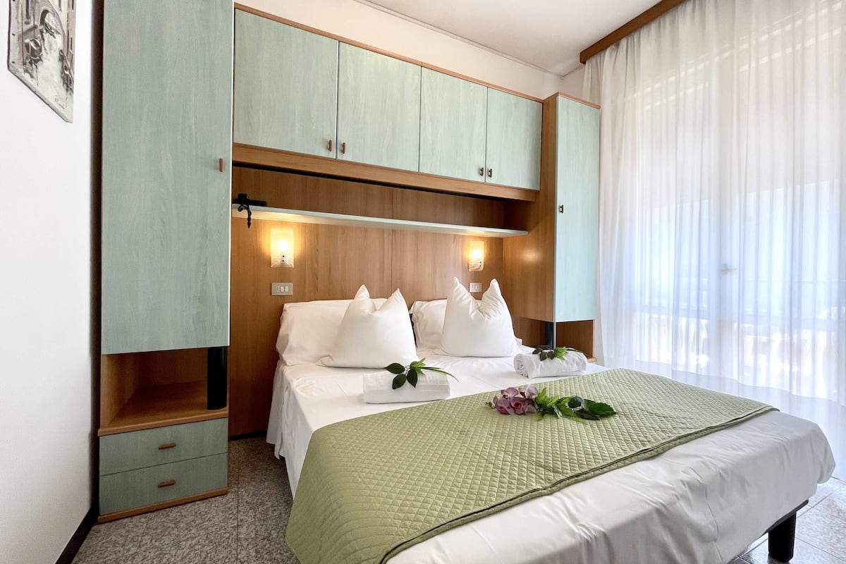 Habitación de hotel con cama, mesita de noche, armario y ventana con cortinas.