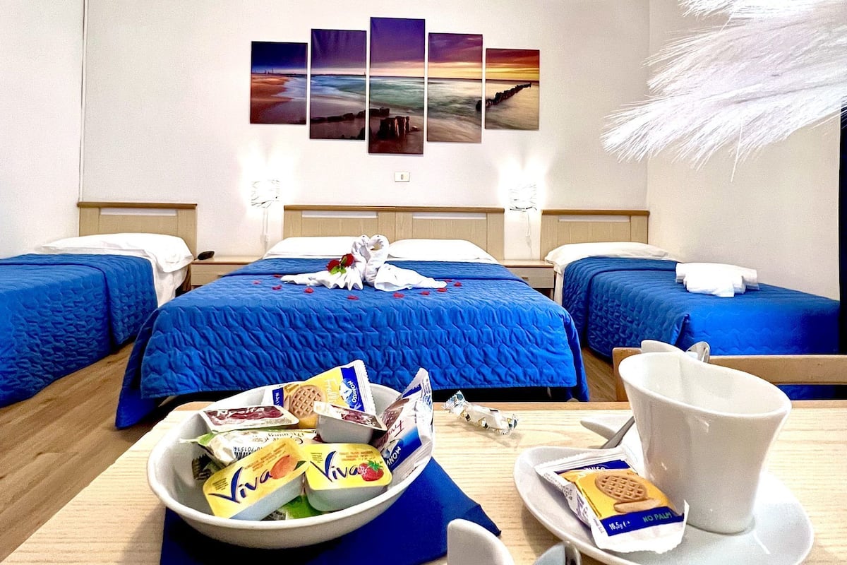 Habitación de hotel con dos camas, una bandeja de desayuno, una taza de café blanca y un cuadro de atardecer en la pared.