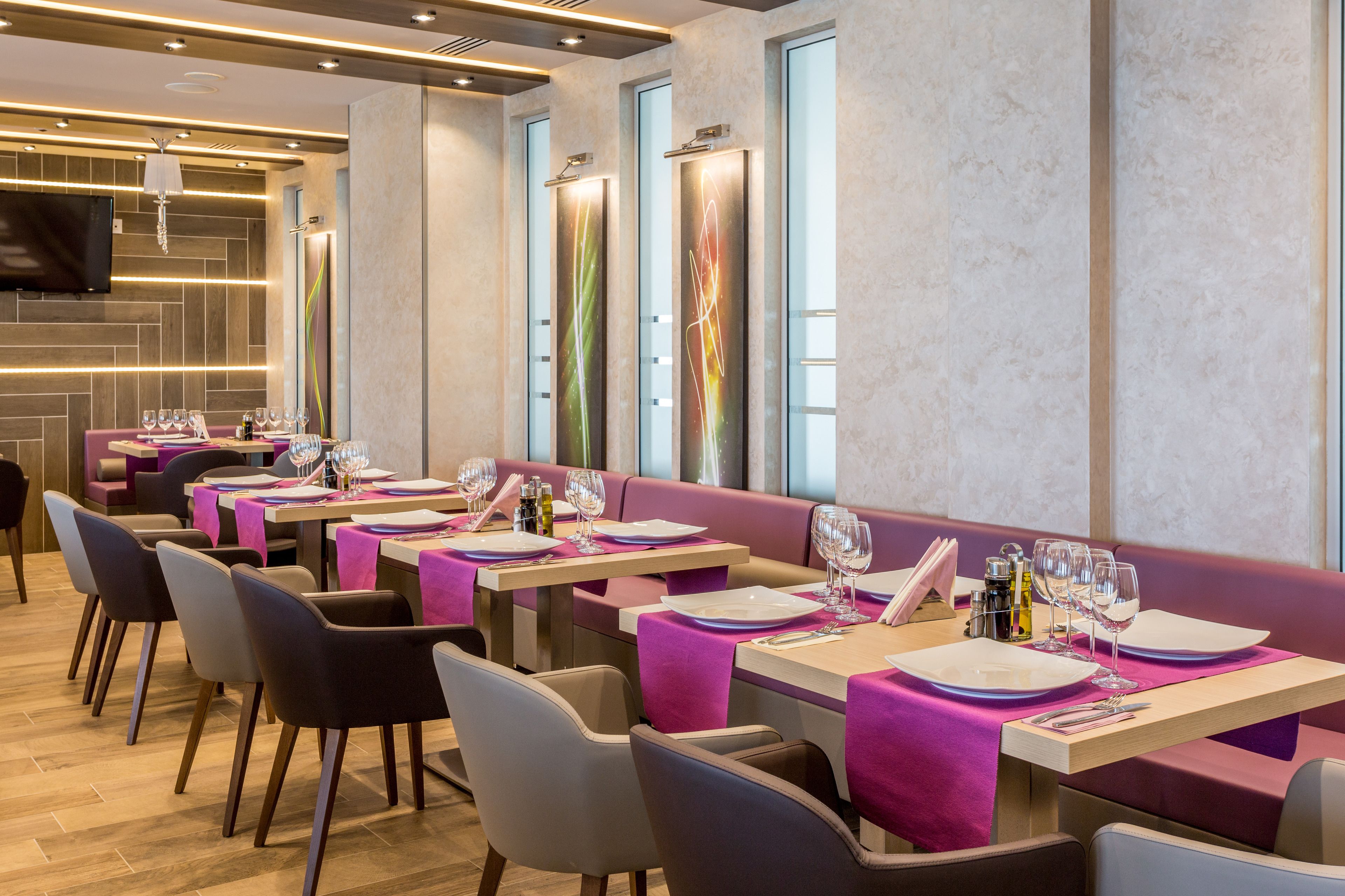 Un restaurante con varias mesas dispuestas para comer, cada una con mantel rosa y cubertería.