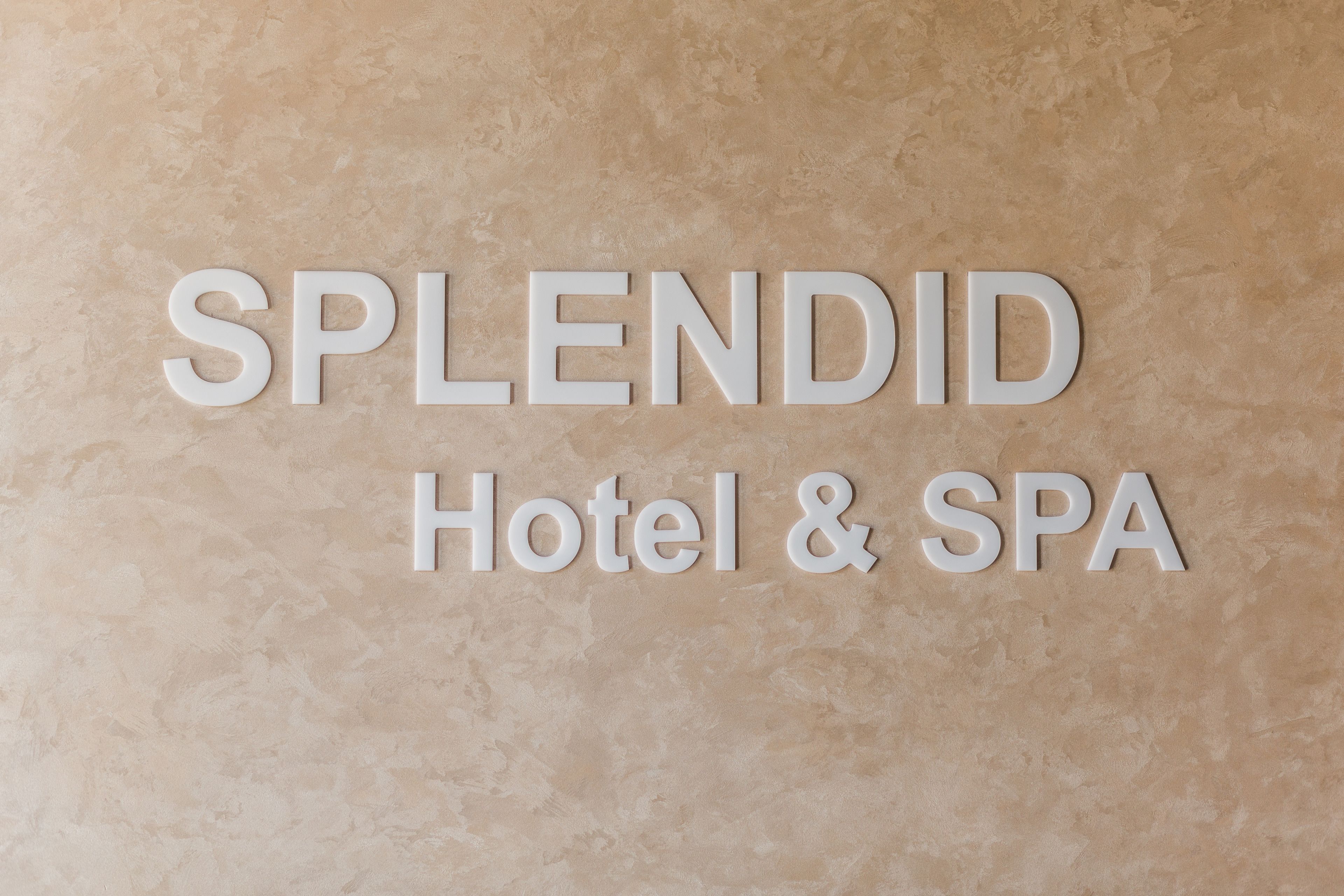 A sign with the words "SPLENDID Hotel & SPA" on a textured beige background.