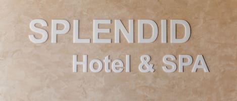A sign with the words "SPLENDID Hotel & SPA" on a textured beige background.