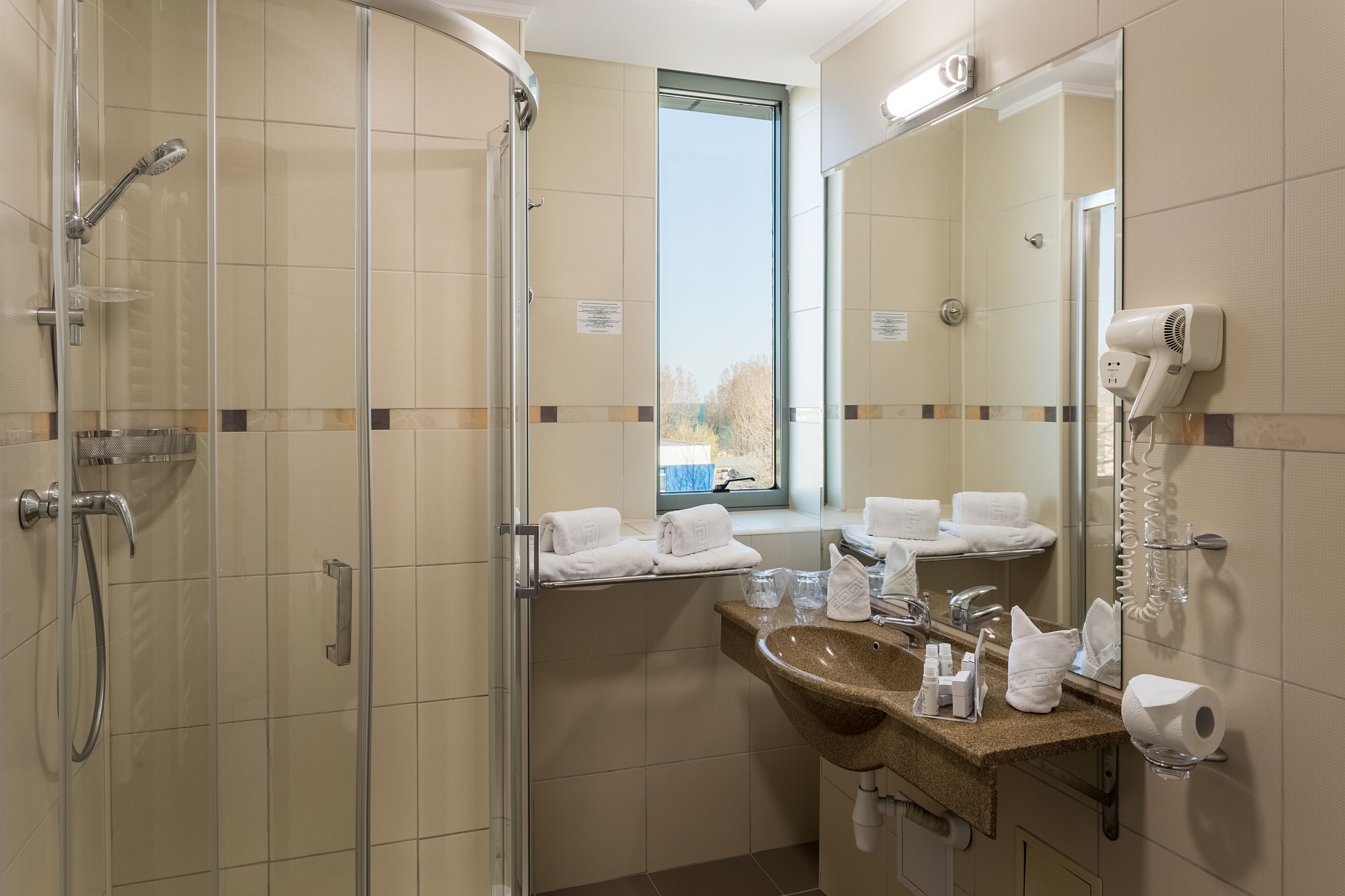 Une salle de bain d’hôtel avec une douche en verre, un lavabo avec des articles de toilette et un miroir équipé d’un sèche-cheveux.
