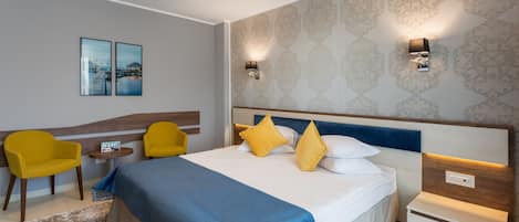 A modern hotel room with a large bed, two yellow chairs, a small table, and a nightstand.