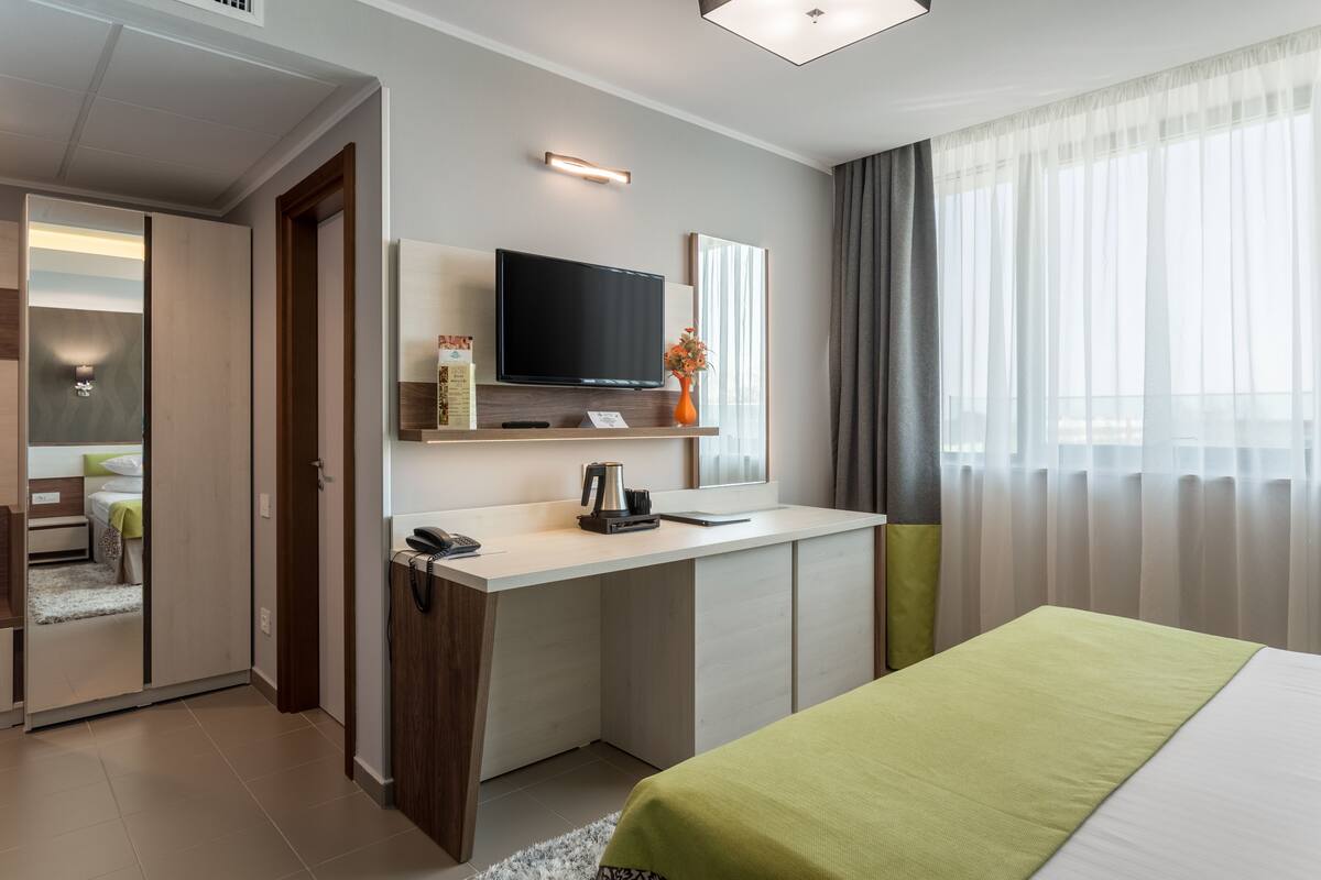 A modern hotel room with a bed, a desk, a television, and a window with curtains.