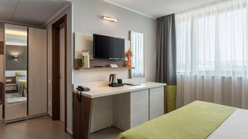 Ein modernes Hotelzimmer mit Bett, Schreibtisch, Fernseher und einem Fenster mit Vorhängen.