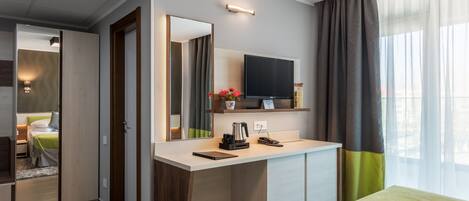 Quarto de hotel com cama, escrivaninha, televisão de tela plana, espelho e janela com cortinas.