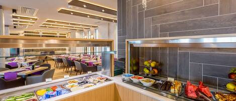 A modern hotel breakfast area with a buffet, seating, and a contemporary design.