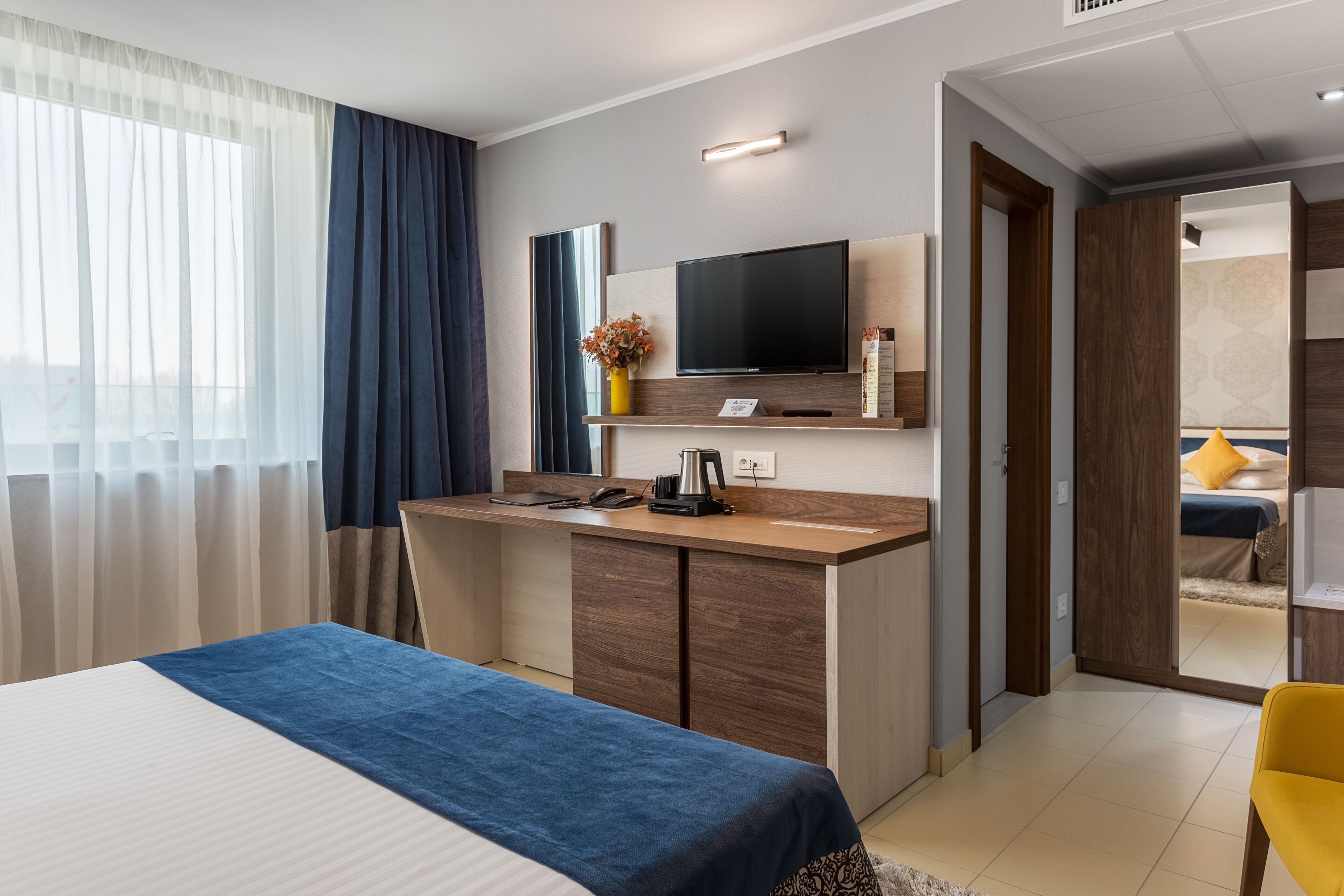 Habitación de hotel con cama, escritorio, televisor de pantalla plana, cafetera y un florero con flores.