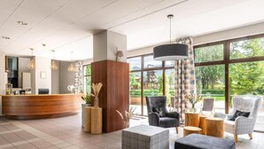 Un vestíbulo amplio con mostrador de recepción, zona de estar y ventanas grandes que ofrecen vistas a la vegetación y montañas.