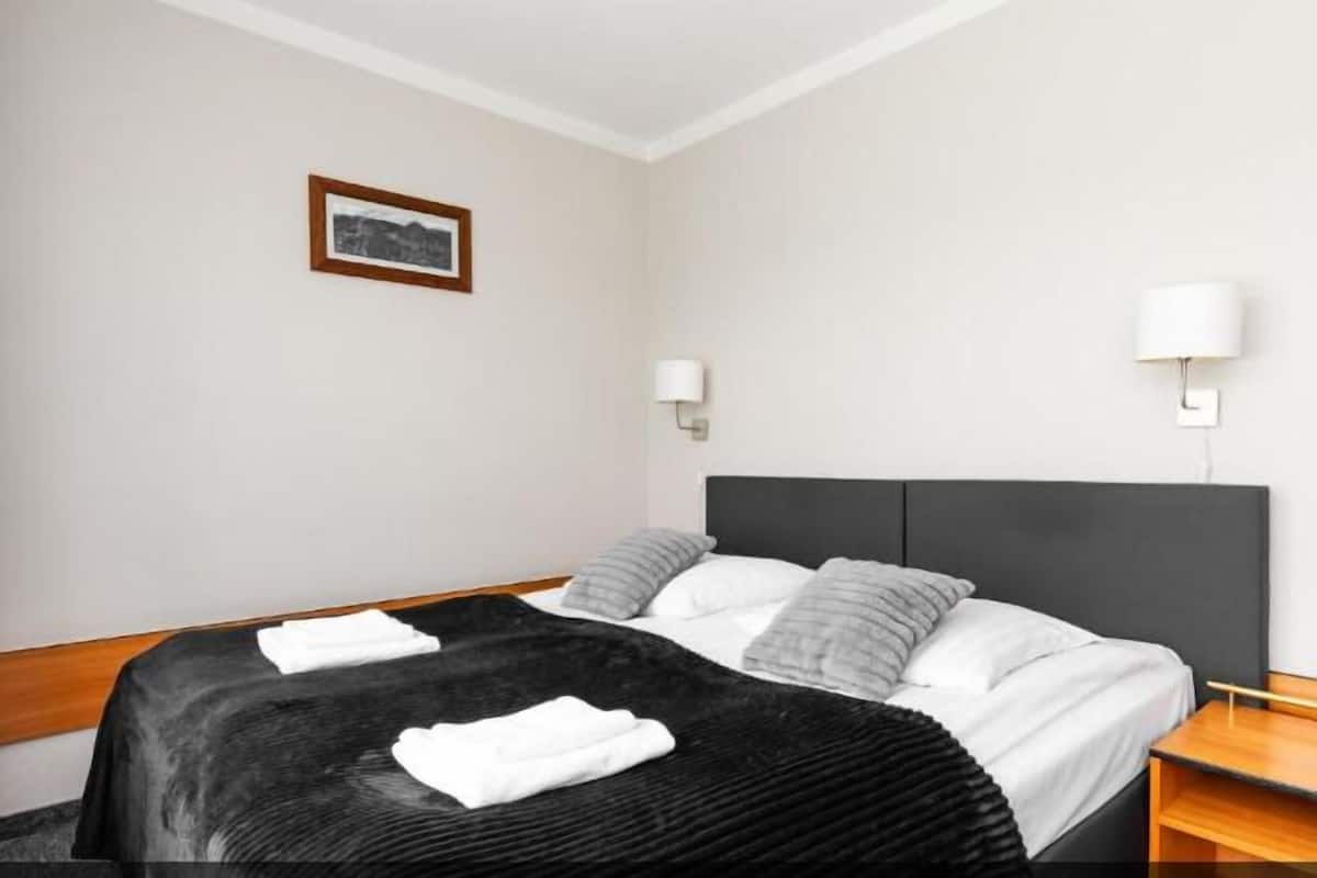 Una habitación de hotel moderna con una cama grande, dos lámparas de noche, un cuadro en la pared y una mesita de noche de madera.