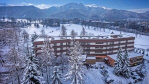 Un hotel de varios pisos con un patio central, rodeado de árboles nevados y montañas al fondo.