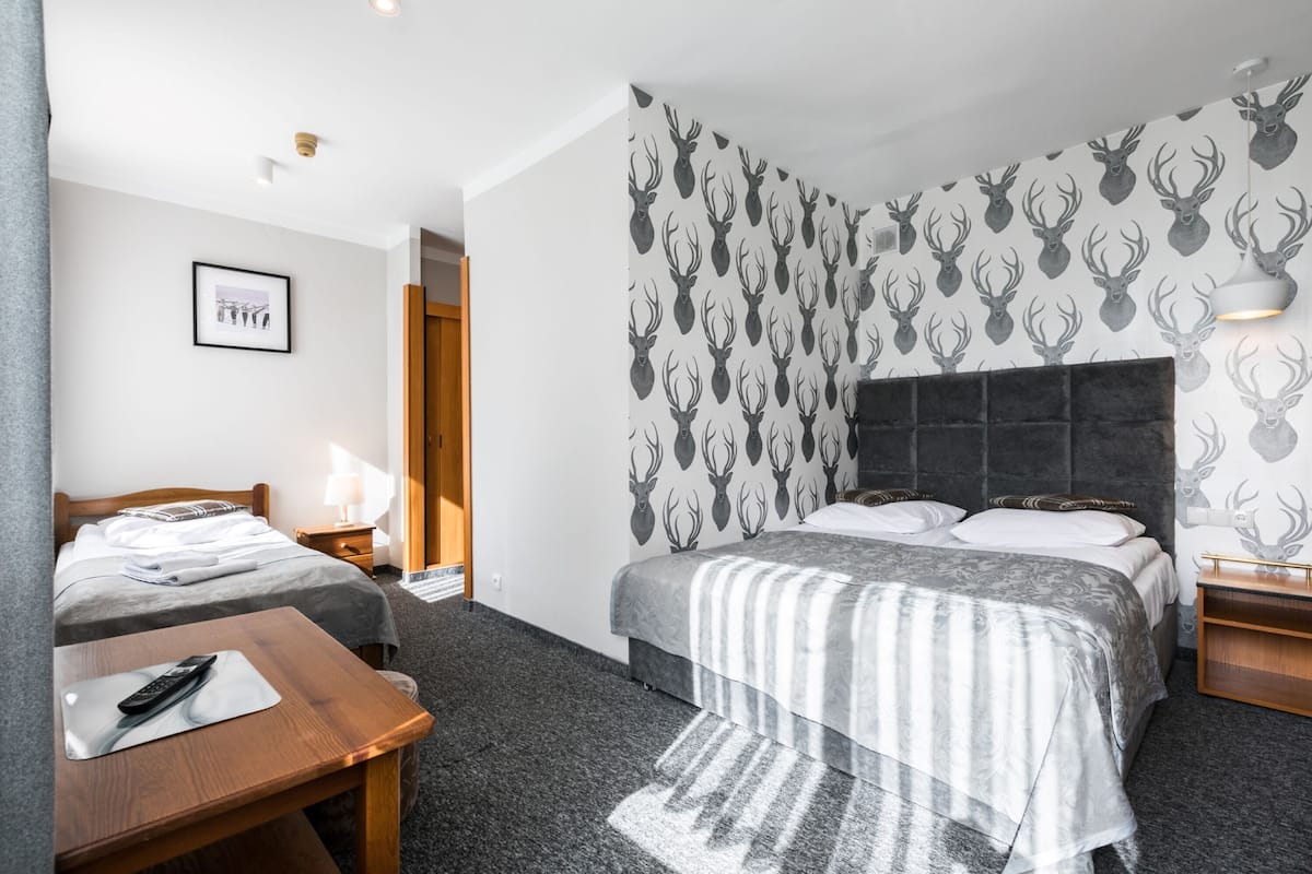 Habitación de hotel con dos camas, un escritorio de madera, un cuadro enmarcado en la pared y un papel tapiz con estampado de cabeza de venado.