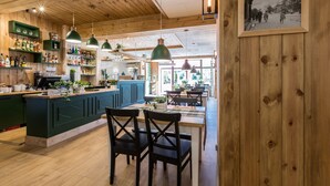 Interior de un restaurante con techos de madera, lámparas colgantes, una zona de bar con estanterías llenas de botellas y un comedor con mesas y sillas.