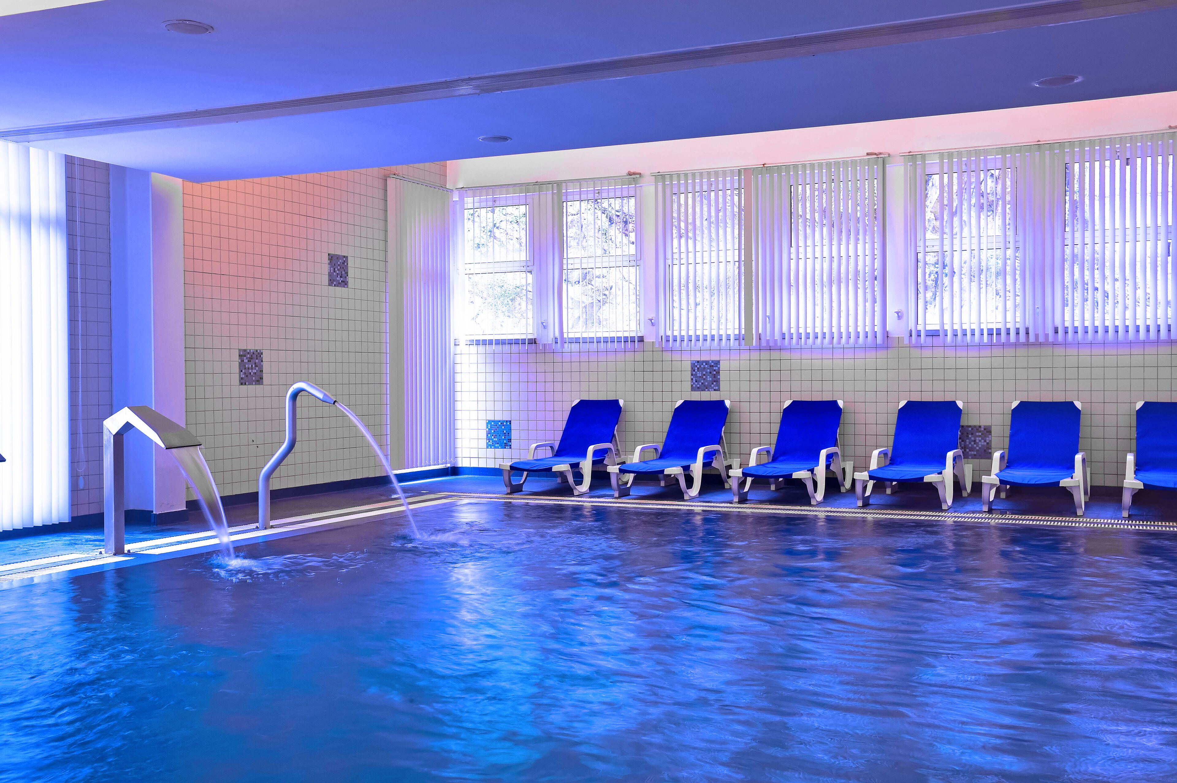 An indoor swimming pool with blue chairs and a water feature.