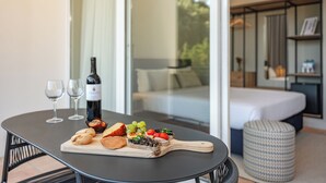 Une table à manger, dressée avec une variété de plats et de verres à vin, se trouve dans une pièce moderne équipée d’un lit et offrant une vue sur la verdure à l’extérieur.