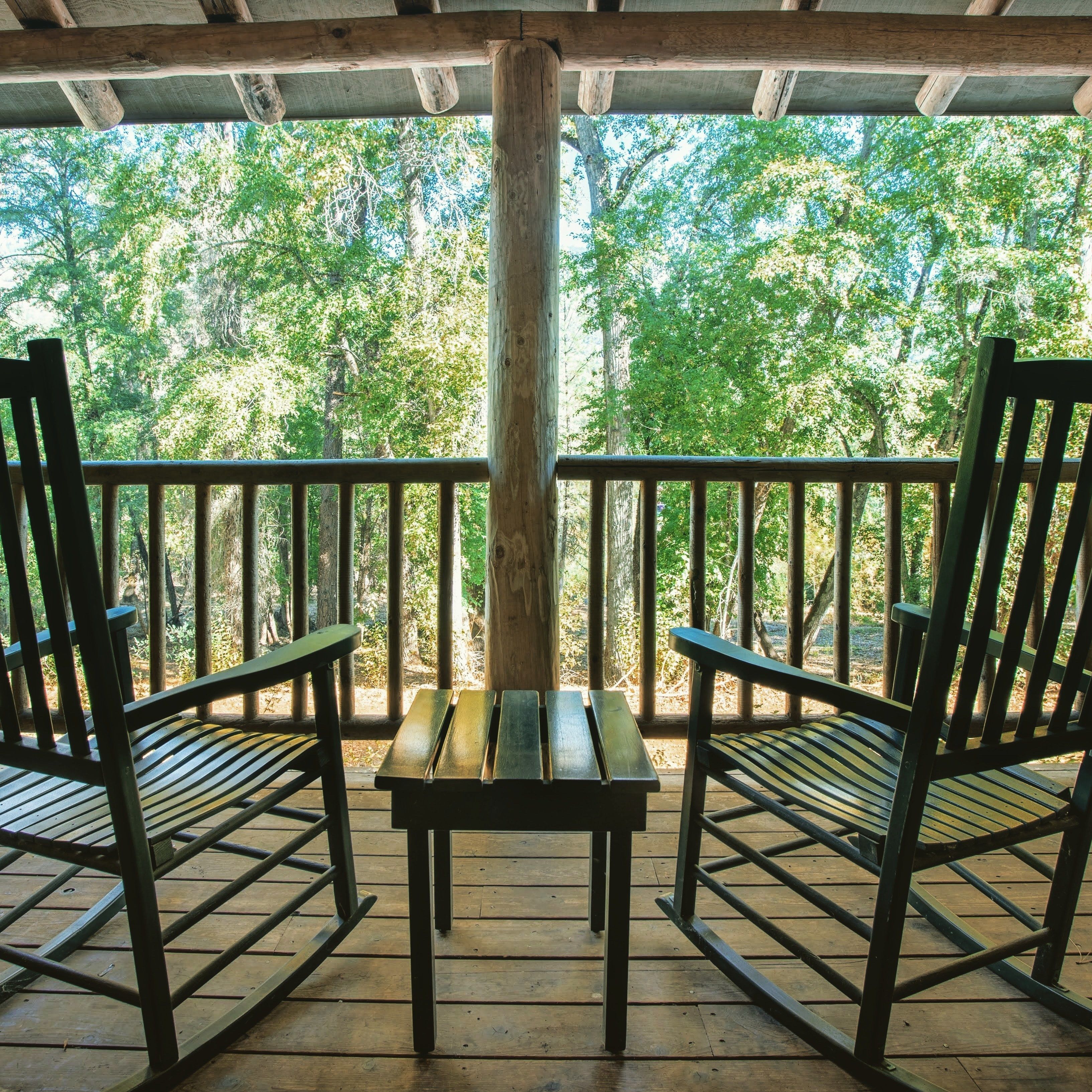 A wooden deck with two chairs and a table, overlooking a forested area.
