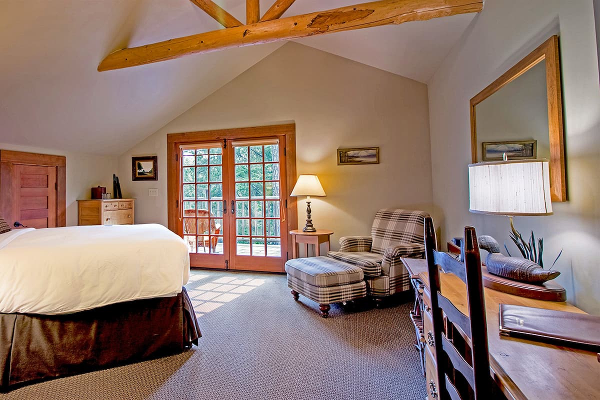 A bedroom with a bed, a chair, a dresser, a lamp, and a large window.