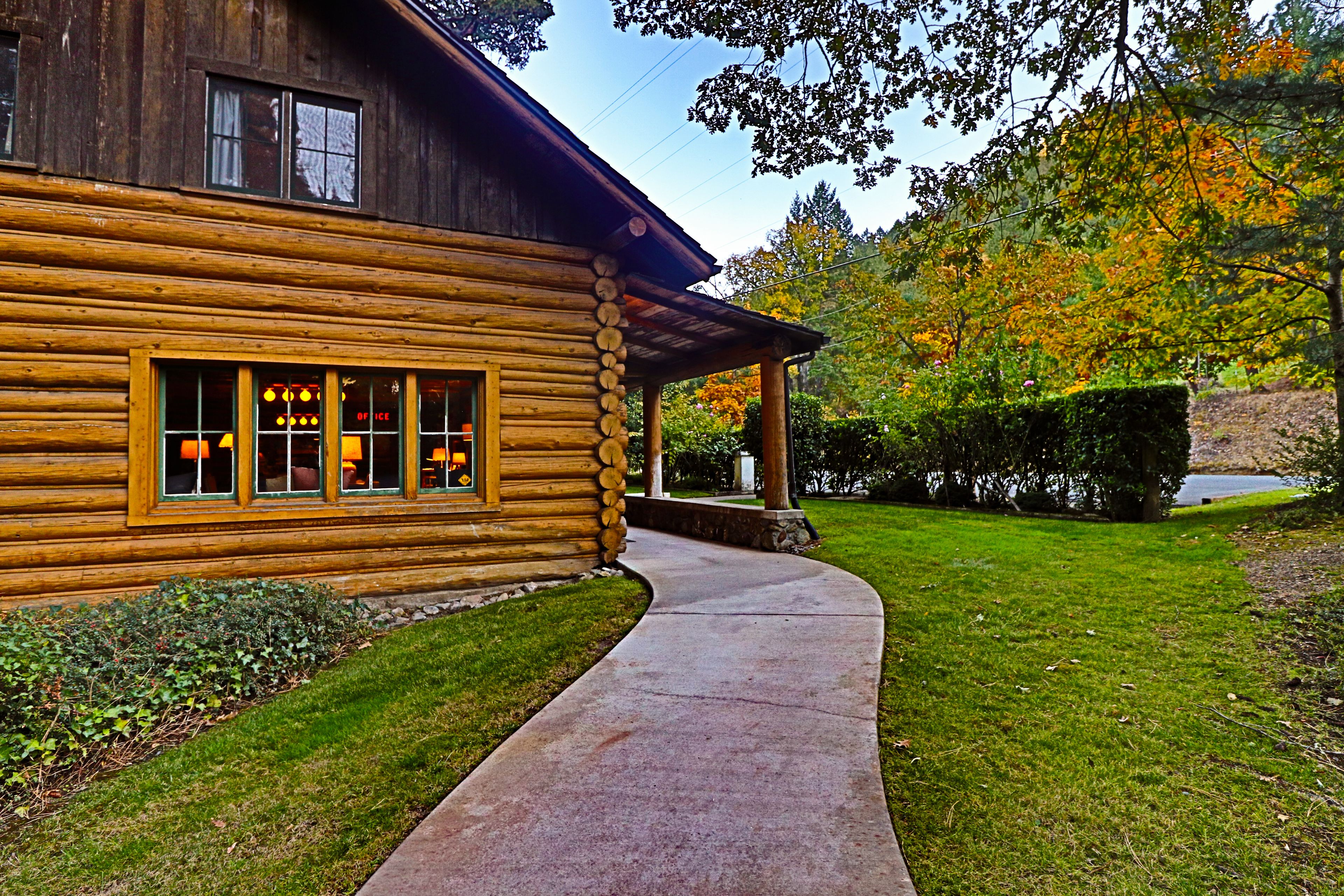 A log cabin with a visible restaurant sign, a paved walkway, and a well-maintained lawn.