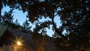 A lodge with a wooden exterior, a deck with chairs, a fire pit, and a sign indicating fishing permits are available. - Weasku Inn (Grants Pass)