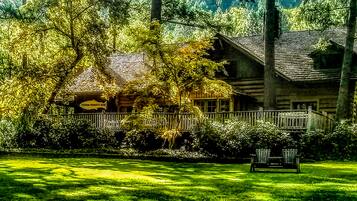 A rustic log cabin with a porch, surrounded by lush greenery and a sign indicating fishing permits.