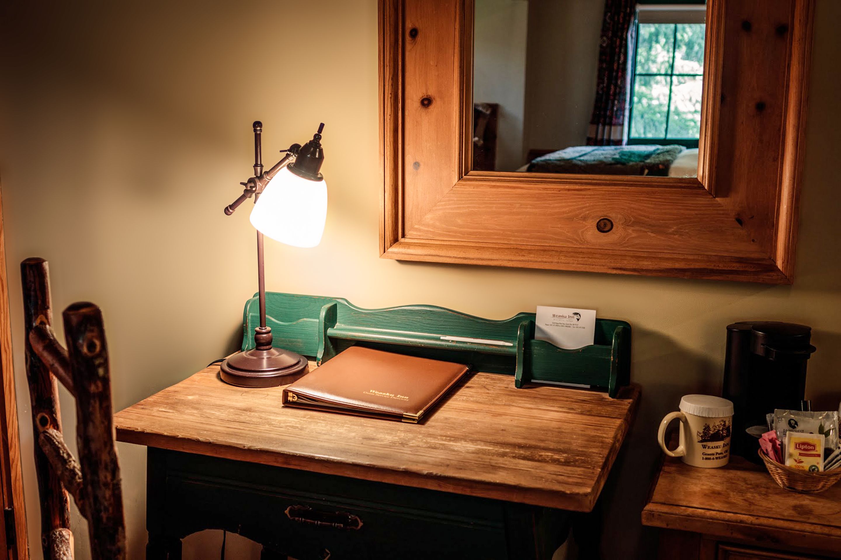 A wooden desk with a lamp, a laptop, a mug, and a basket of items.