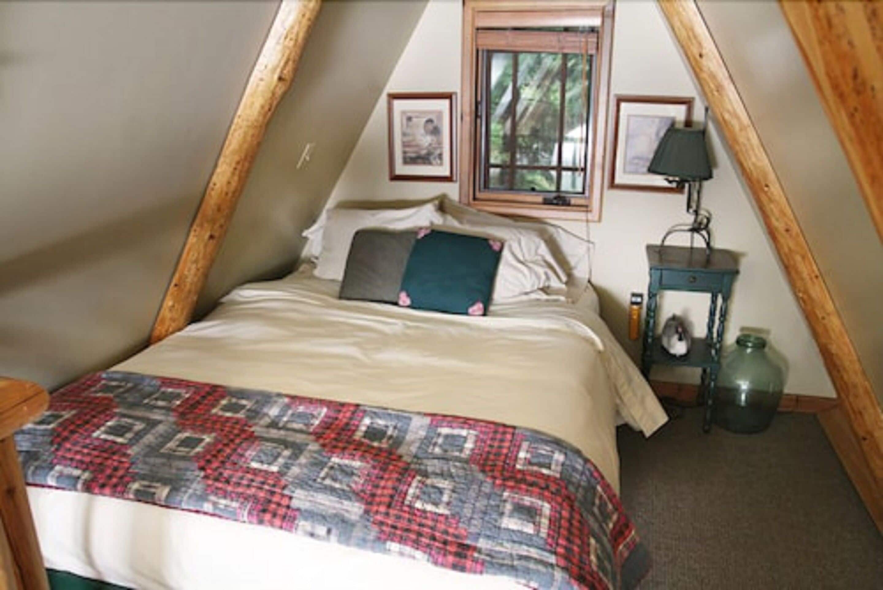 Ein gemütliches Schlafzimmer im Dachgeschoss mit einem Bett, einem Nachttisch, einer Lampe und einem gerahmten Bild an der Wand.