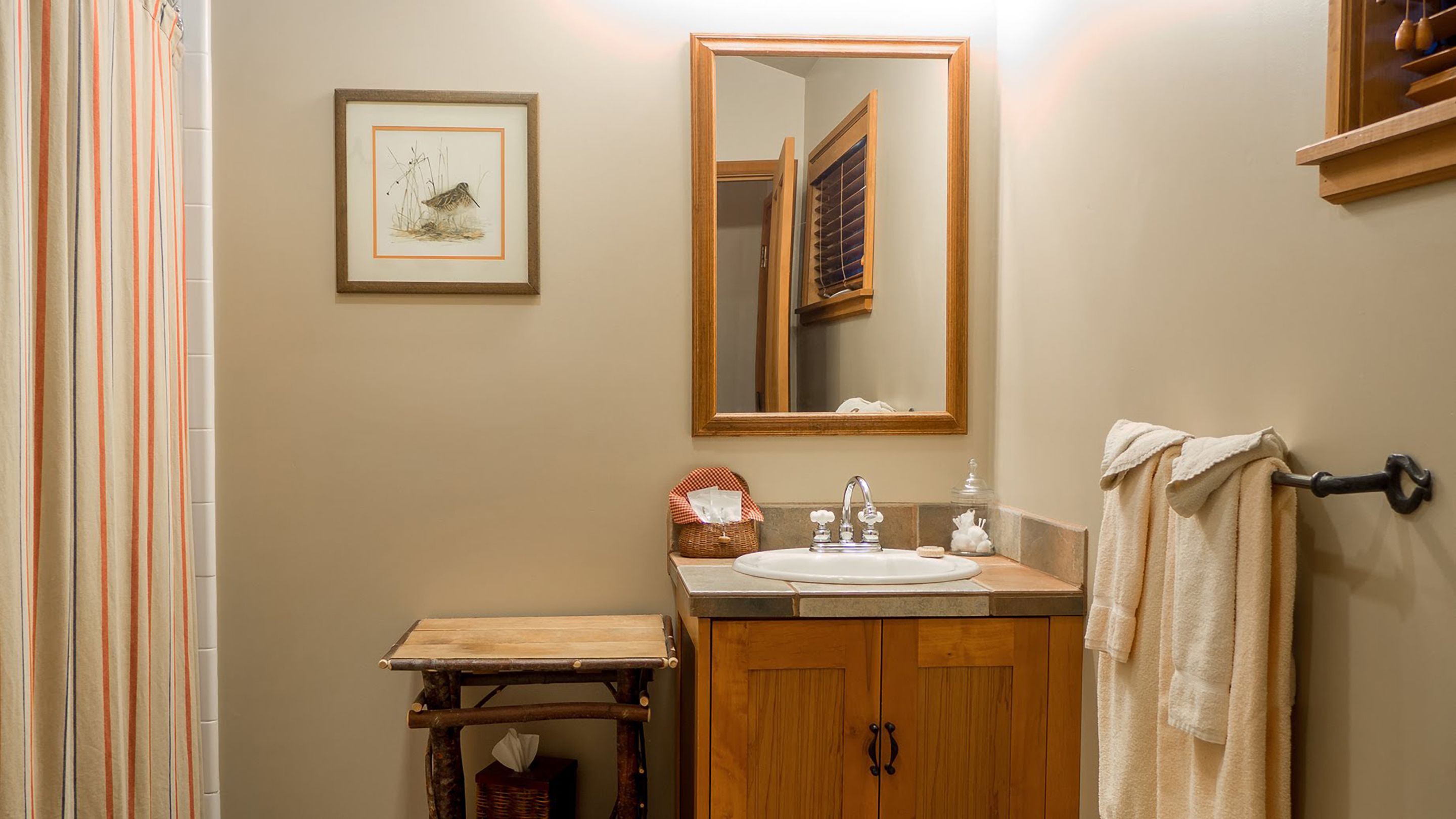 A bathroom with a wooden vanity, a mirror, a framed picture, and a towel rack.