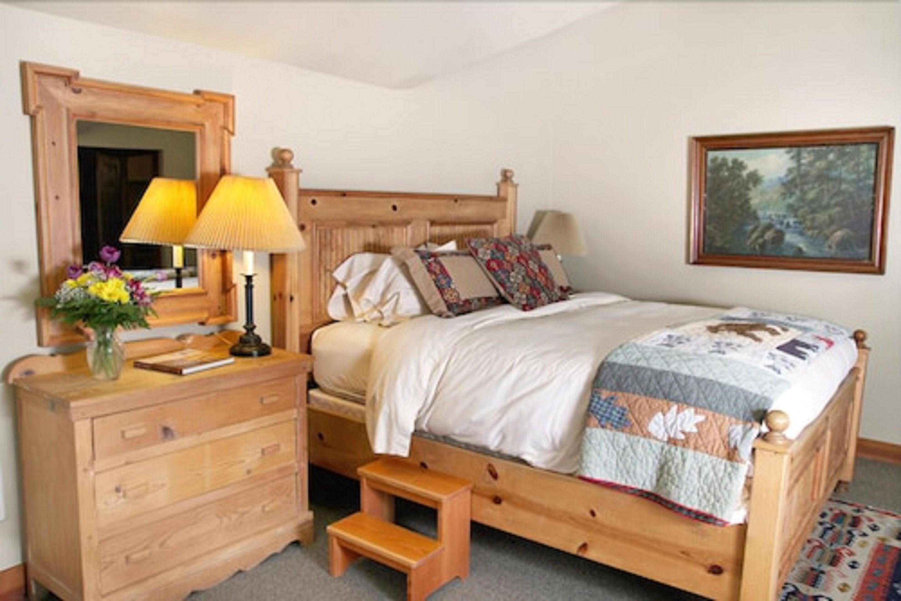A bedroom with a wooden bed, a nightstand with a lamp, a dresser, and a mirror.