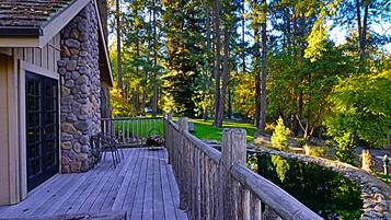 A wooden deck with stone walls, a pond, and a forested area.