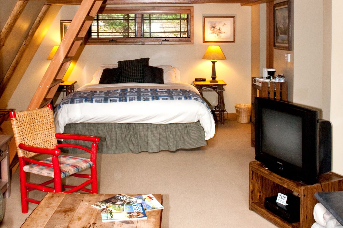 A loft bedroom with a bed, a television, a dining table, and a chair.
