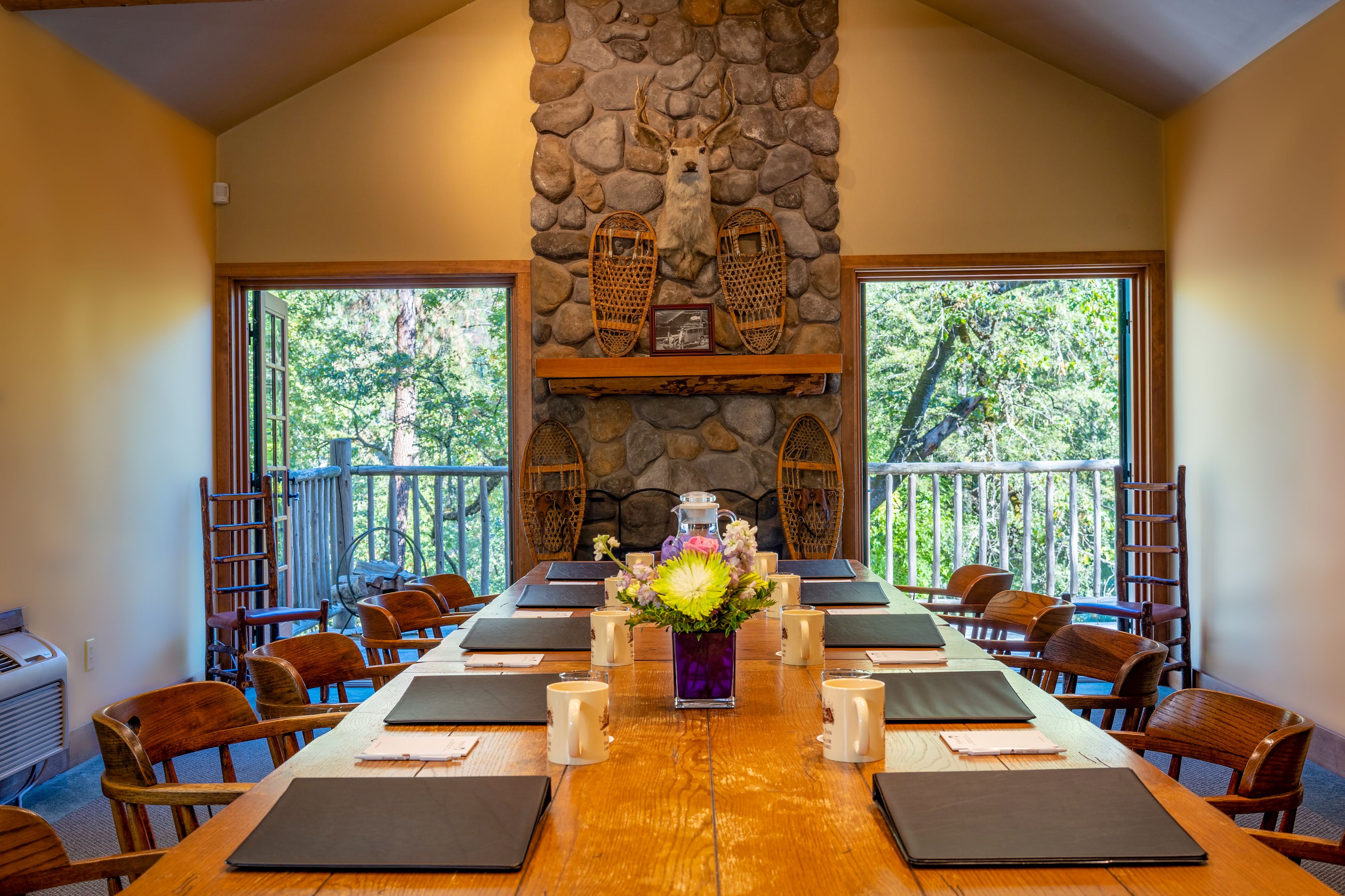 A conference room with a stone fireplace, wooden chairs, and a long table set for meetings.