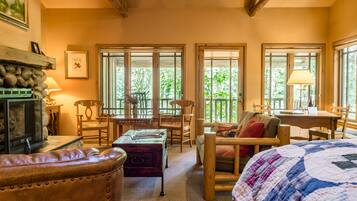 A cozy room with a fireplace, wooden furniture, and large windows offering a view of greenery.
