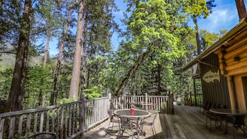 Une terrasse en bois avec des sièges extérieurs, entourée de grands arbres et surplombant un ciel dégagé.