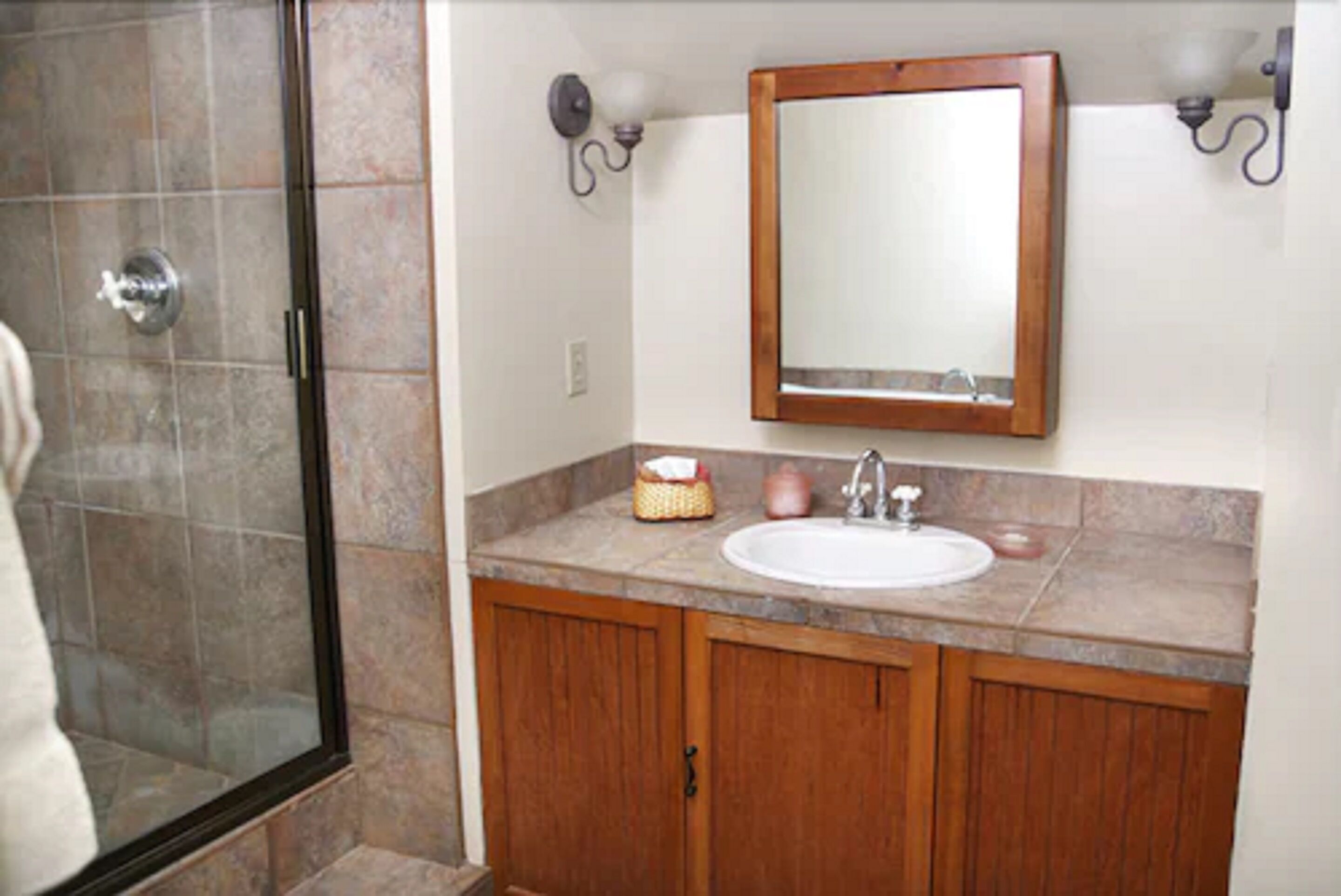 A bathroom with a glass shower enclosure, a wooden vanity with a sink, and a mirror above the vanity.