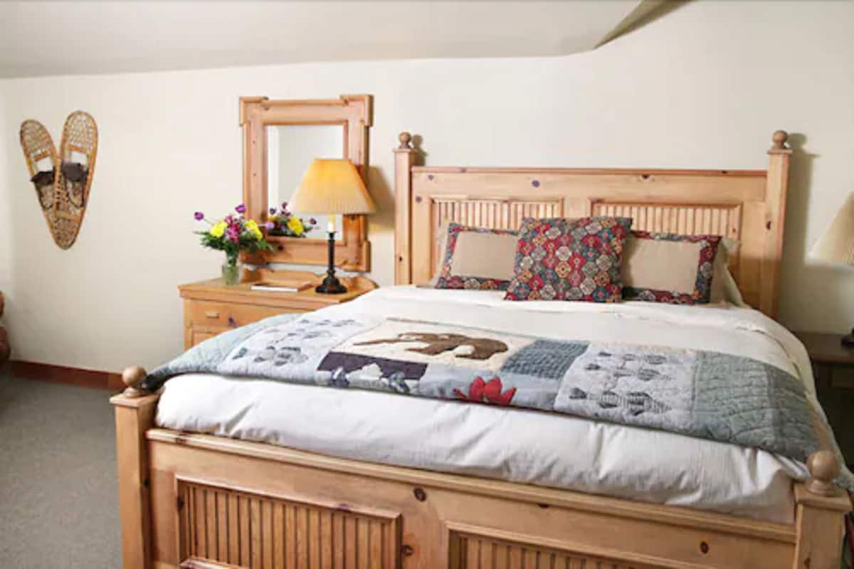A wooden bed with a floral quilt, a bedside table with a lamp, and a mirror on the wall.