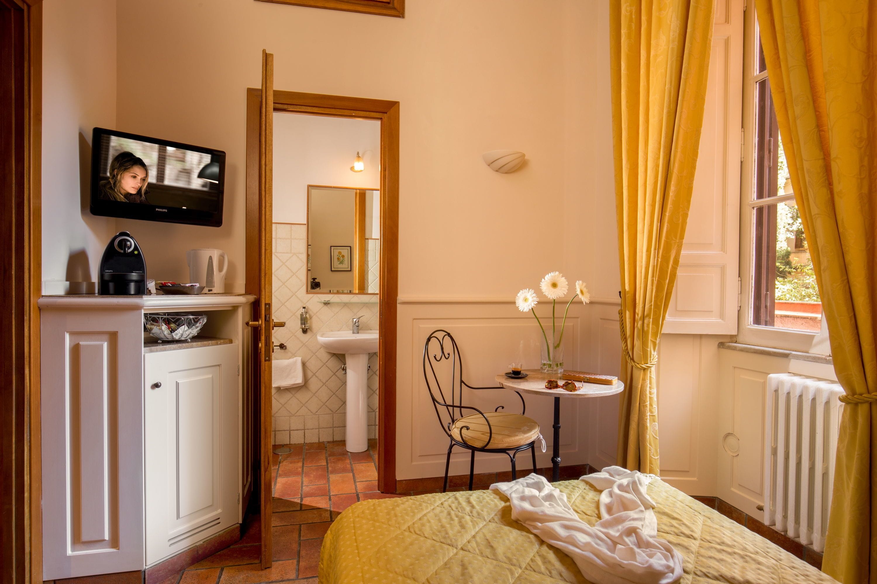 Une chambre d’hôtel avec un lit, une télévision, un lavabo, une chaise et une fenêtre avec des rideaux.