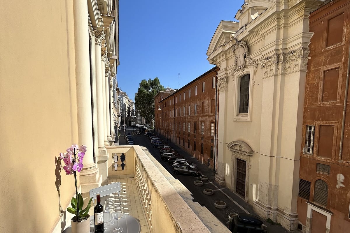 A balcony with a table, chairs, a potted orchid, and a bottle of wine.