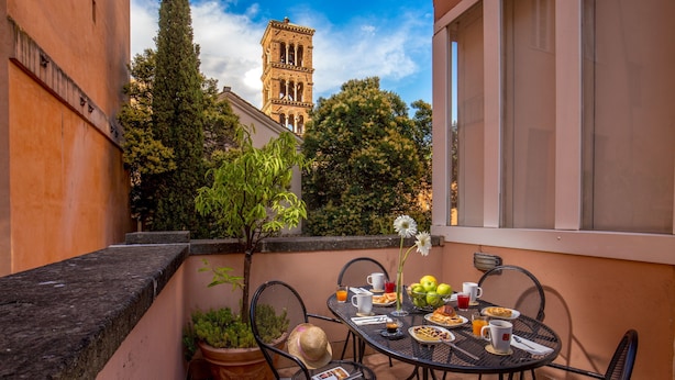 A balcony with a table set for breakfast, potted plants, and a view of a historic tower. - Aenea Superior Inn (Rome)