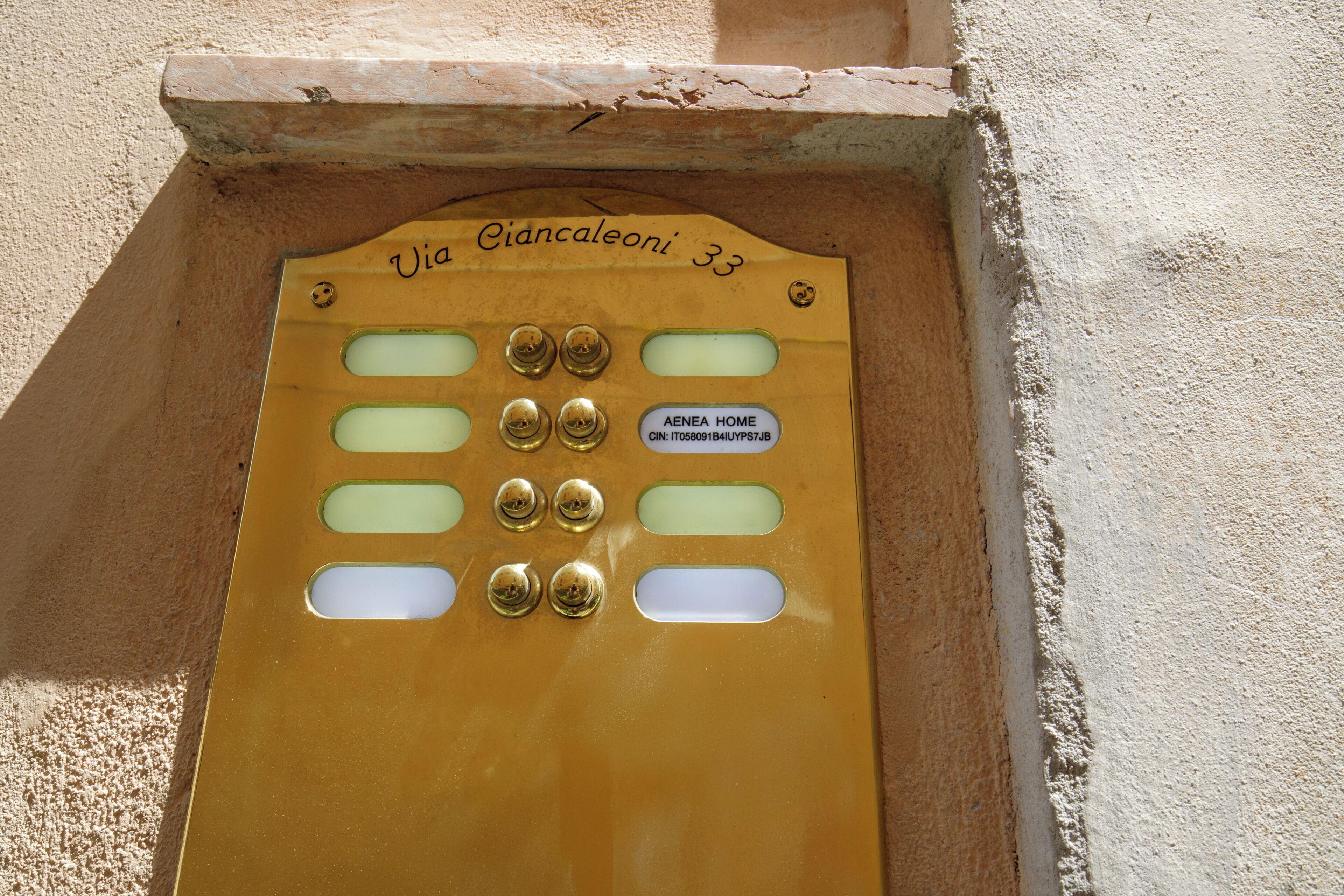 A gold-colored door with a nameplate reading "Via Giancalèoni 33" and "AENE HOME" along with a CIN number.