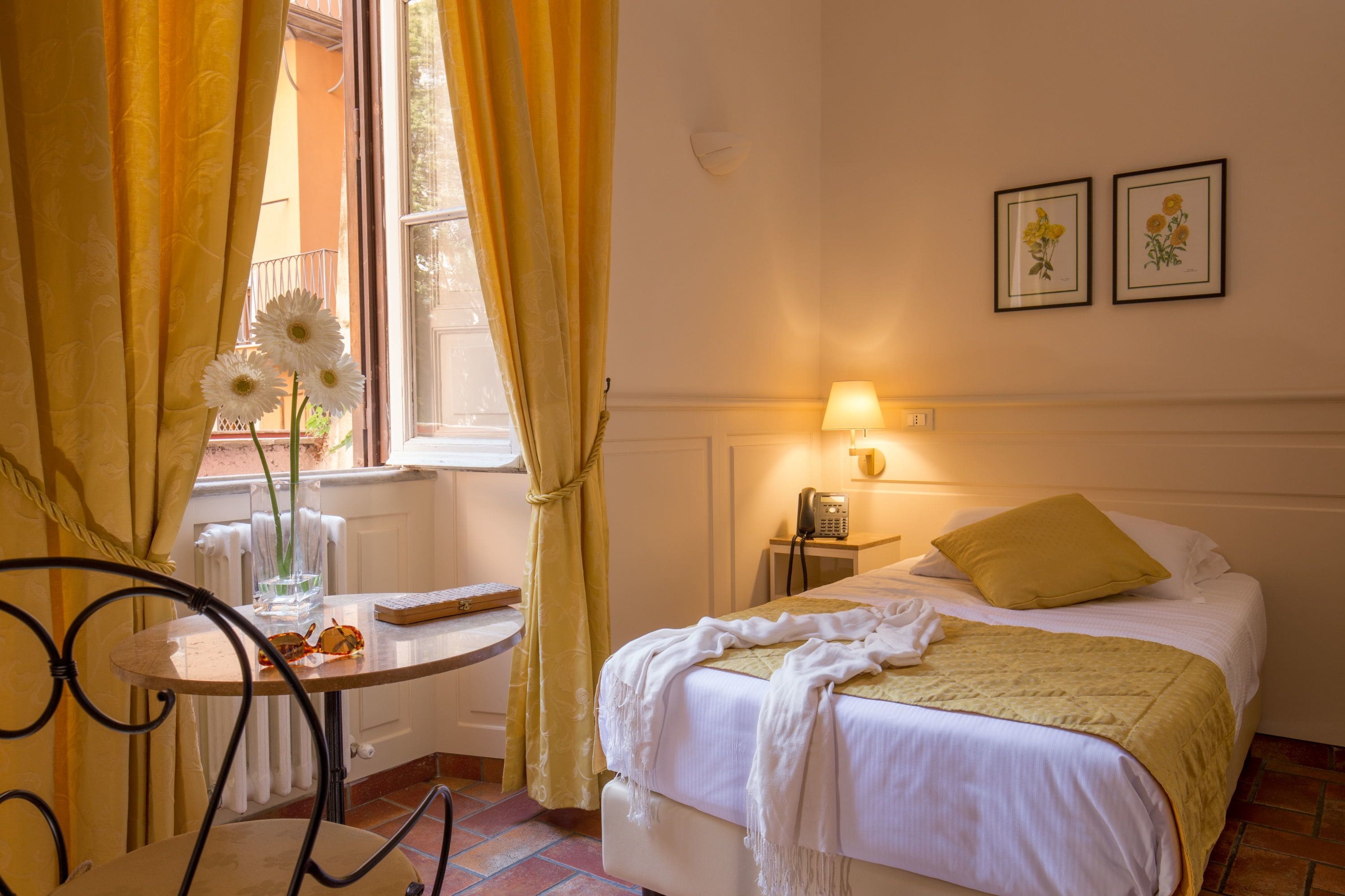 A hotel room with a bed, a bedside table, a lamp, and a window with curtains.
