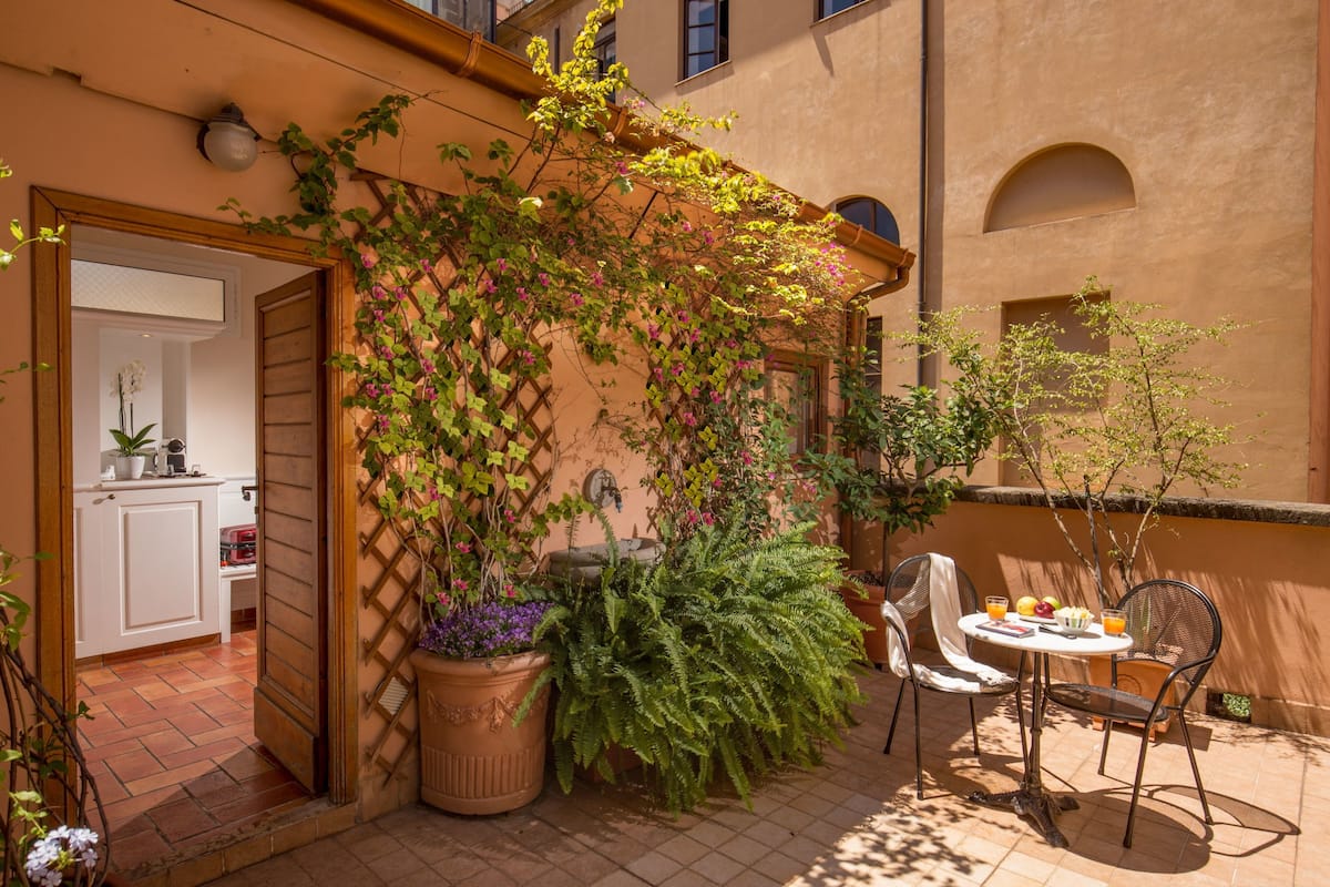 A patio with a table and chairs, surrounded by potted plants and a wooden trellis.