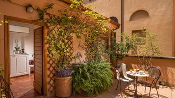 Eine Terrasse mit Tisch und Stühlen, umgeben von Topfpflanzen und einem hölzernen Spalier.