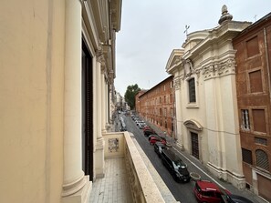 A narrow street lined with parked cars and historic buildings with classical architecture.