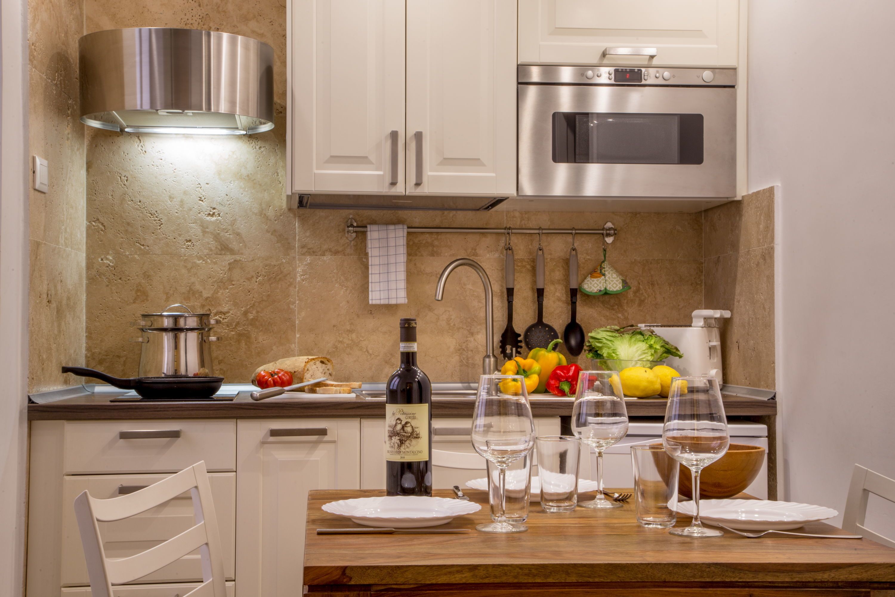 A modern kitchen with white cabinets, stainless steel appliances, and a dining area set with wine glasses and plates.