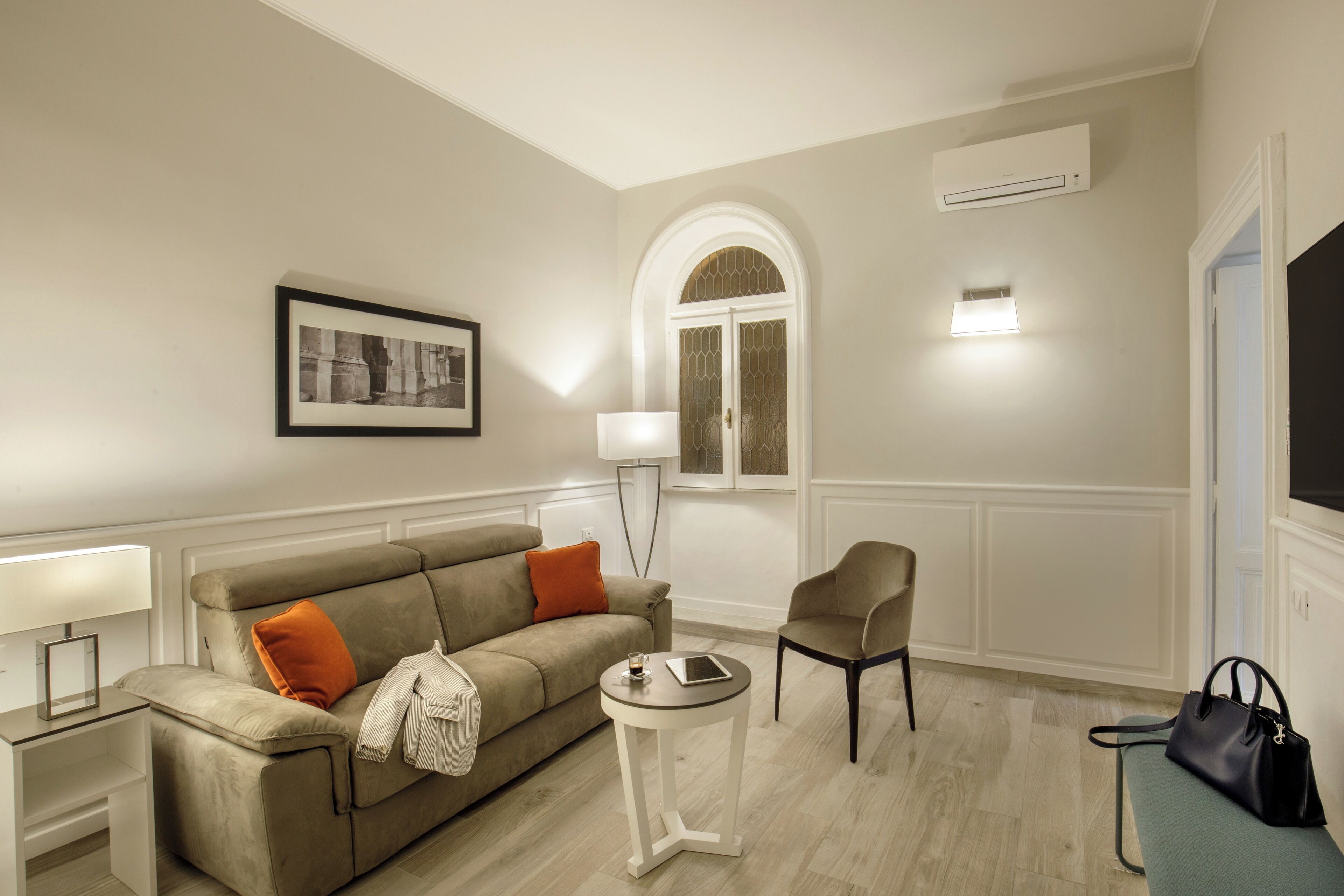 Un salon avec un canapé beige, une petite table ronde, un fauteuil, une lampe et un téléviseur.