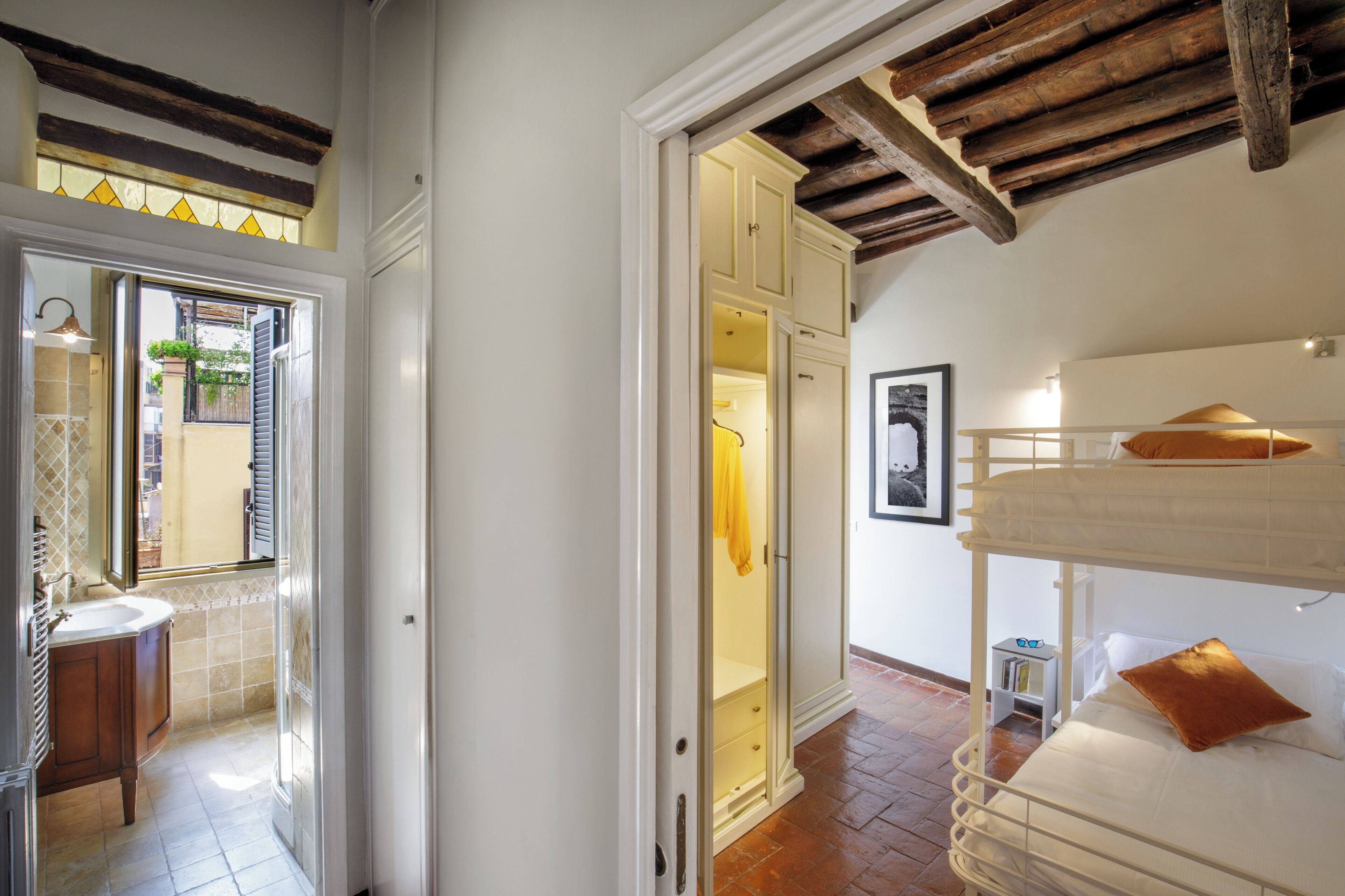 A room with a bunk bed, a bathroom with a sink, and a door leading to another room.