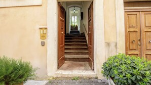 A staircase leading to a wooden door, with a small plant on the left and a wall-mounted device on the right. - Aenea Superior Inn (Rome)