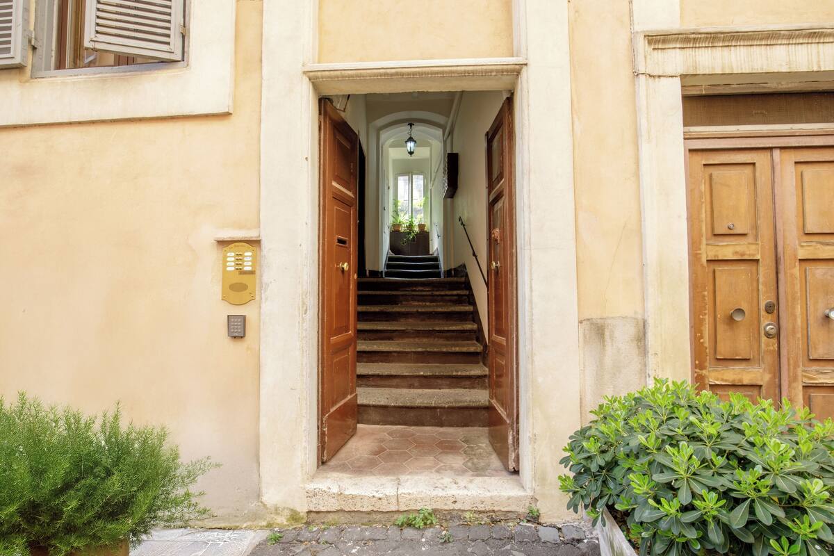 A staircase leading to a wooden door, with a small plant on the left and a wall-mounted device on the right.