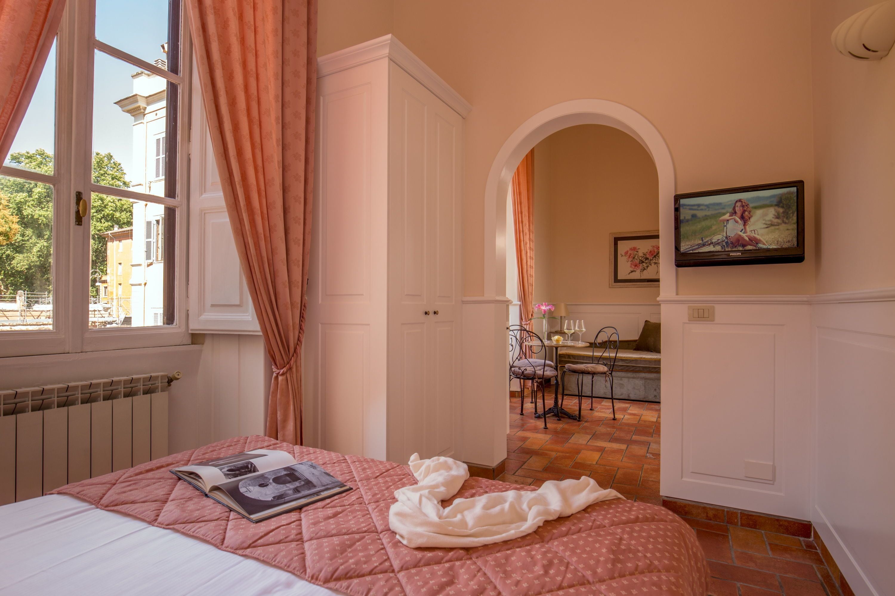 Une chambre à coucher avec un lit, une fenêtre avec des rideaux, un tableau au mur et une vue sur l’extérieur.